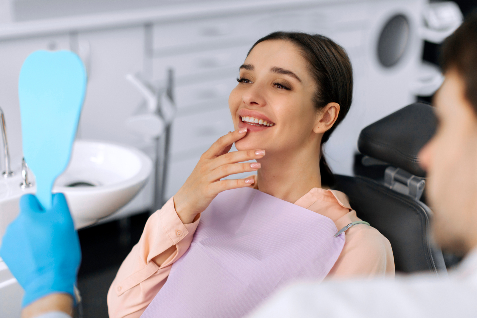 Smiling patient checking her new smile in a mirror at the dentist